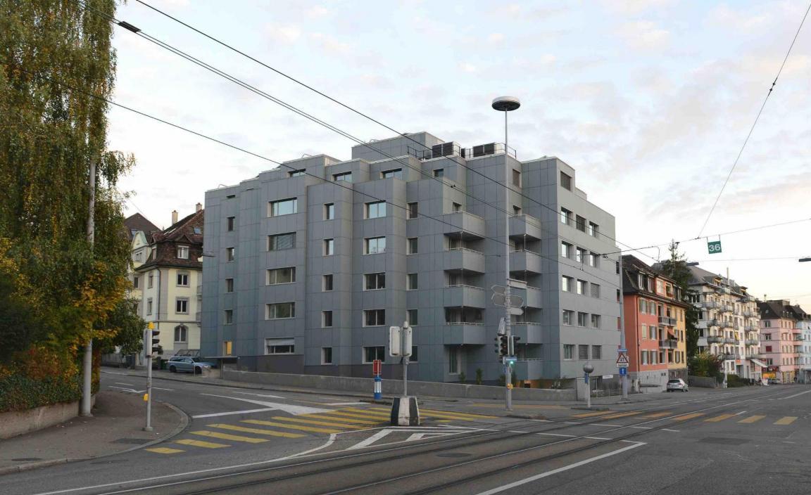 Ein Wohnblock an einer Strassenkreuzung in der Stadt Zürich mit neuer grauer Solarfassade.