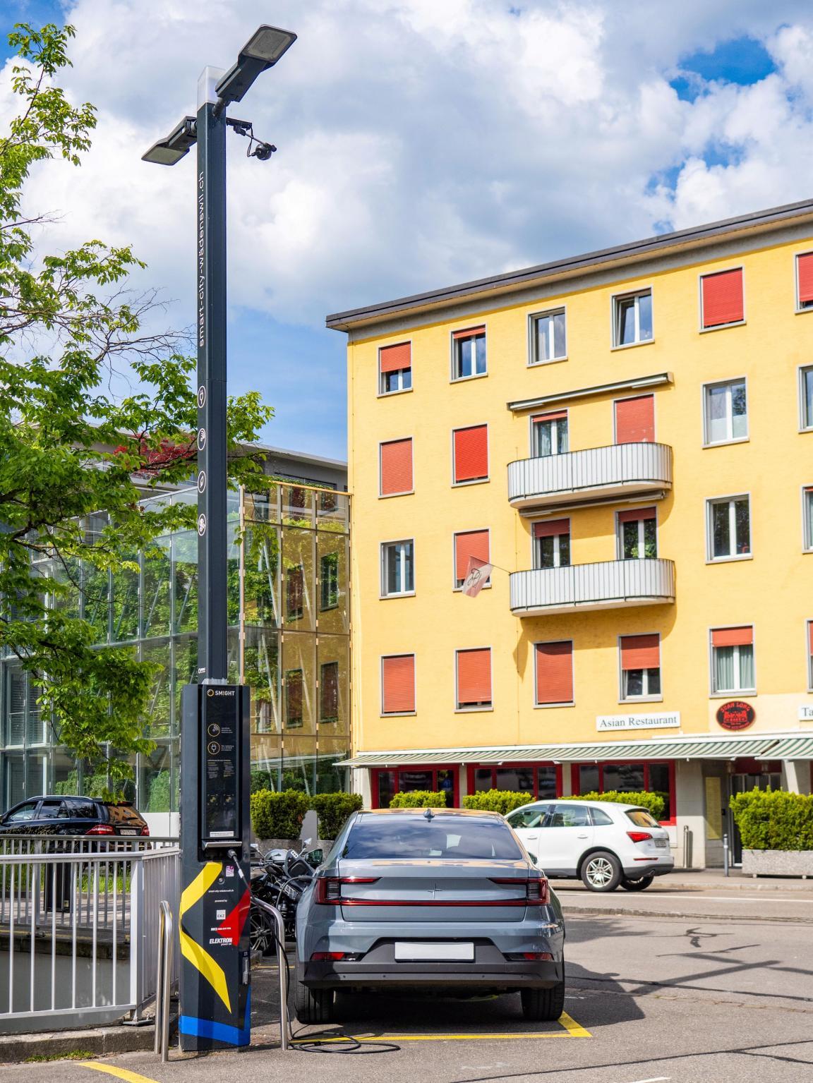 Ein Elektroauto an einer Ladestation an einem Laternenmast. 