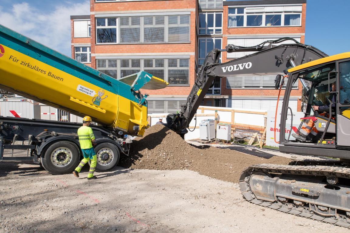 Ein elektrischer Bagger schafft das Kies weg, das von einen E-Lastwagen auf der Baustelle angeliefert wurde. 