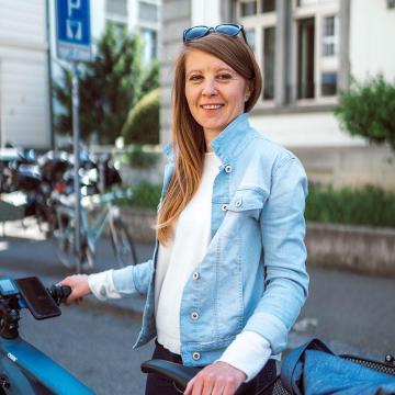 Viktoria Herzog steht hinter einem Velo und trägt eine weisse Bluse und eine Jeansjacke. 