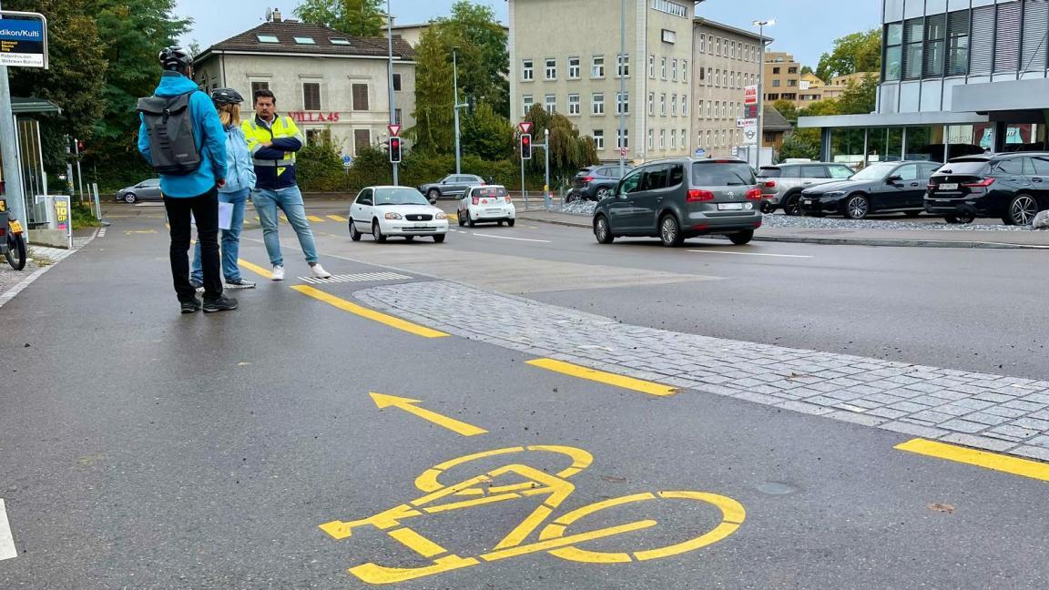 Auf einem gelb markierten Radweg stehen drei Personen und unterhalten sich über die Planung von Radwegen. 