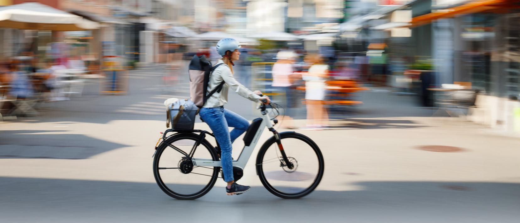 Vor einem verwischten Hintergrund fährt eine Frau mit Helm auf einem E-Bike.
