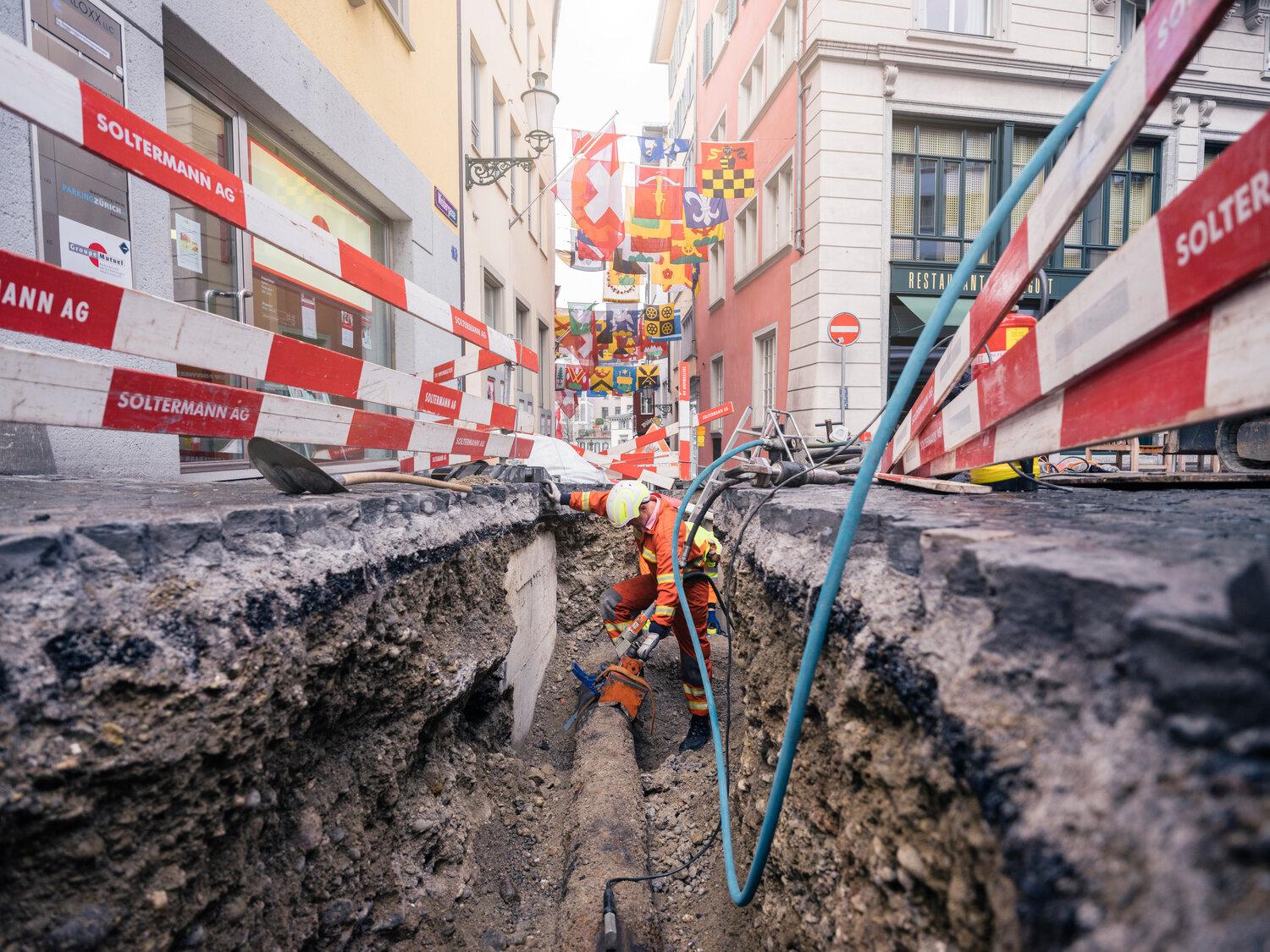 Ein grosse offene Baugrube im Niederdorf. Ein Bauarbeiter arbeitet an einer Gasleitung. 