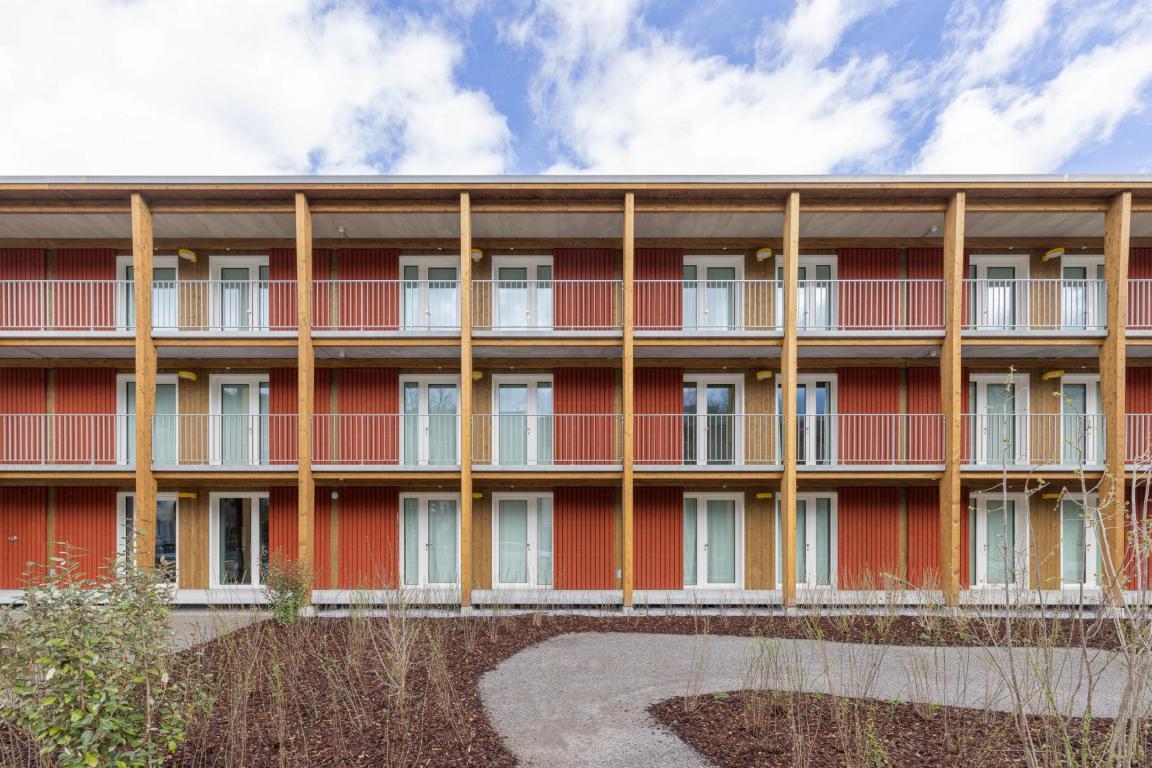 Frontalansicht des Asylzentrums Adliswil. Rote Fassade mit vielen Holzmodulen. 