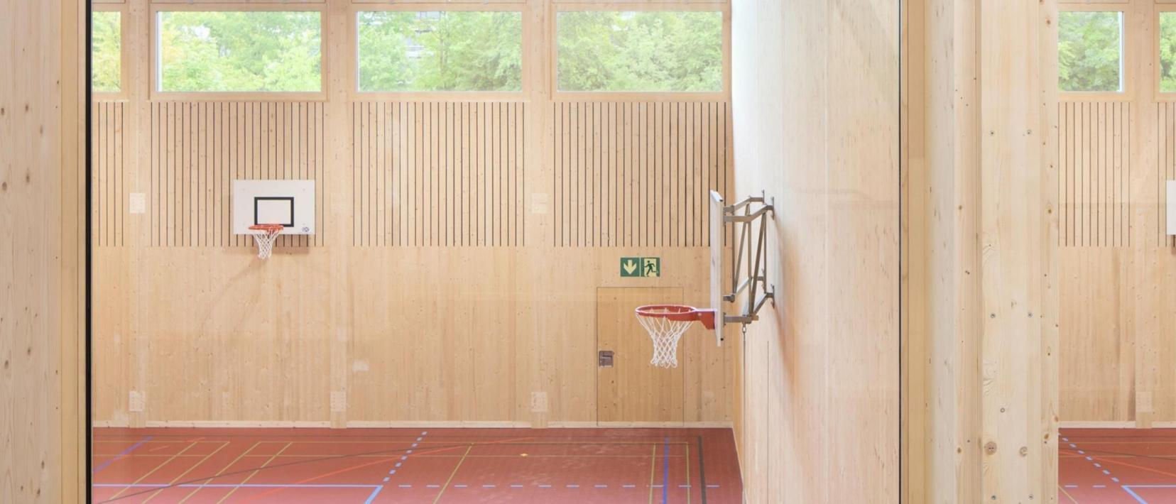 Innenansicht der provisorischen Turnhallen, die aus hellem Holz gebaut sind.