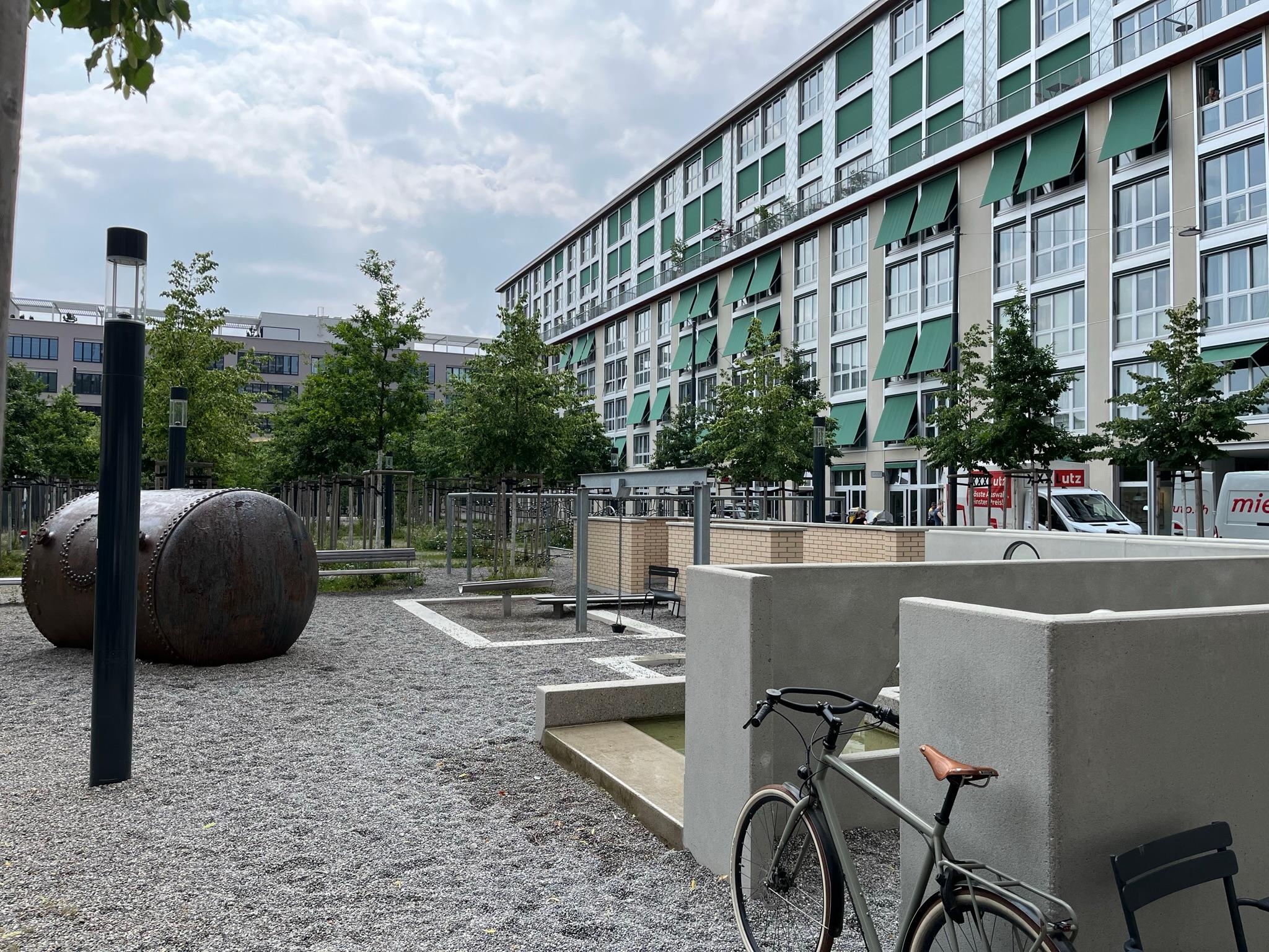 Das Foto zeigt einen Teil des Sulzer Areals mit seinen hohen Mehrstöckigen Wohn- und Gewerbeblöcken. Zwischen den Gebäuden hat es ein Kiesplatz mit vielen Sitzgelegenheiten und ein Raster von neu gepflanzten Bäumen