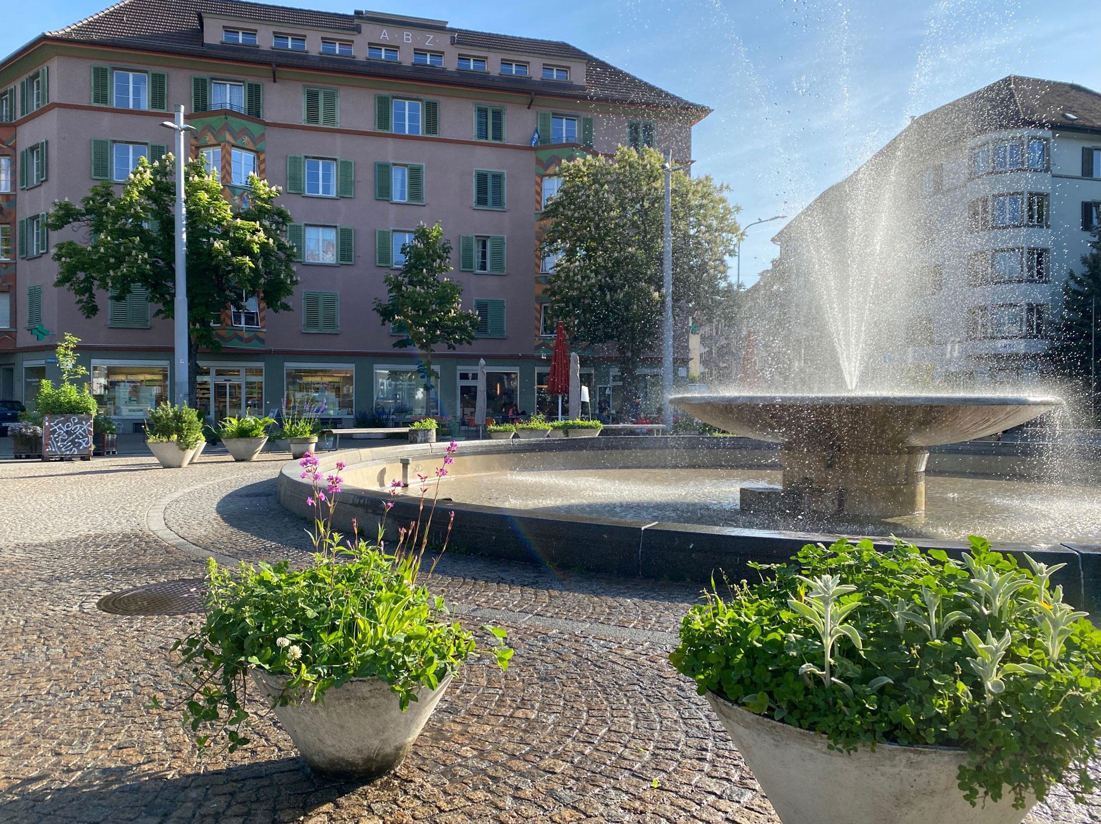 Das Foto zeigt den Springbrunnen in der Mitte des Bullingerplatzes in Zürich und wie die Luft voller Wassertröpfchen ist.