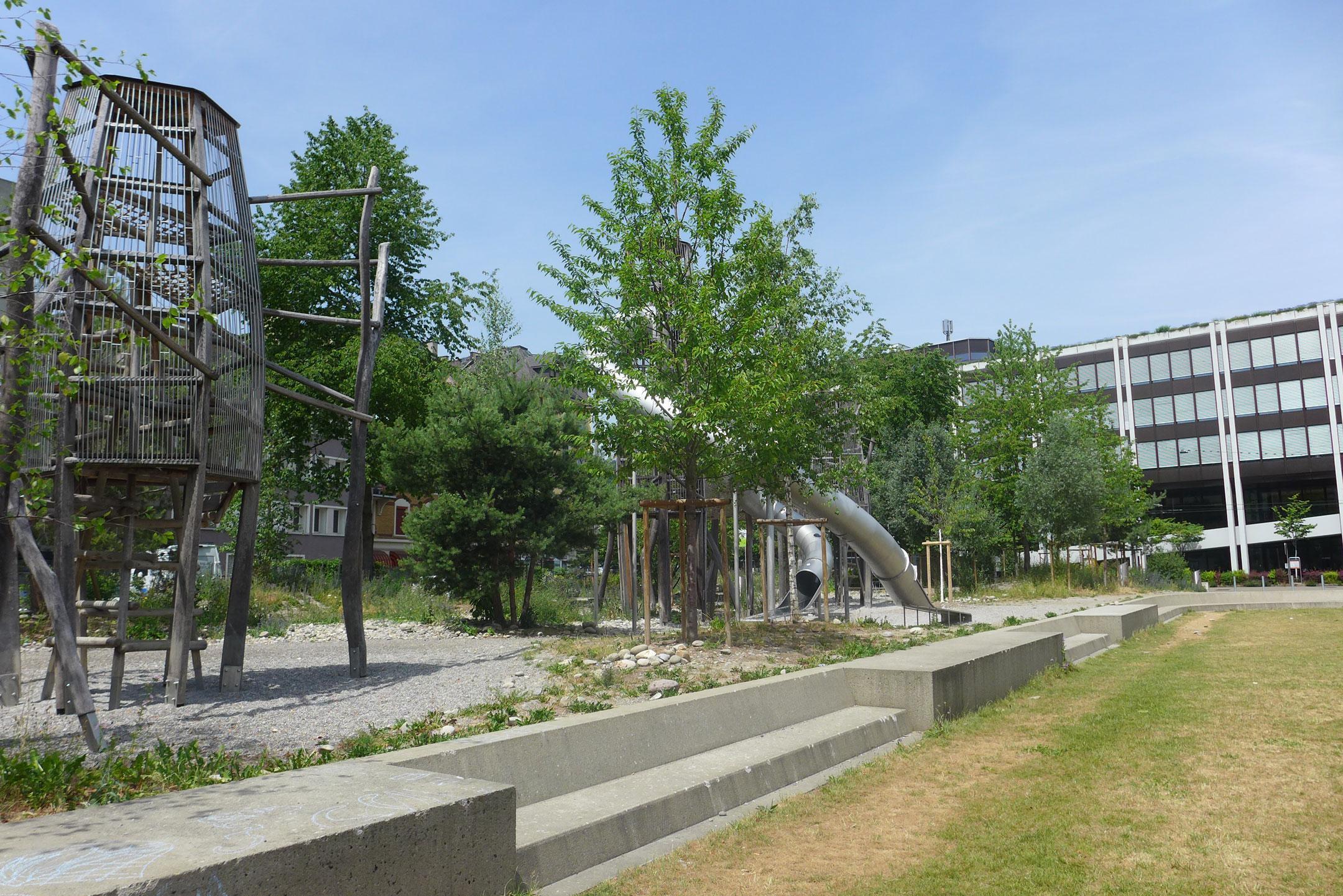 Das Foto zeigt ein Spielturm aus Holz und zwei grosse Röhrenrutschen. Im Vordergrund hat es eine grosse Spielwiese.