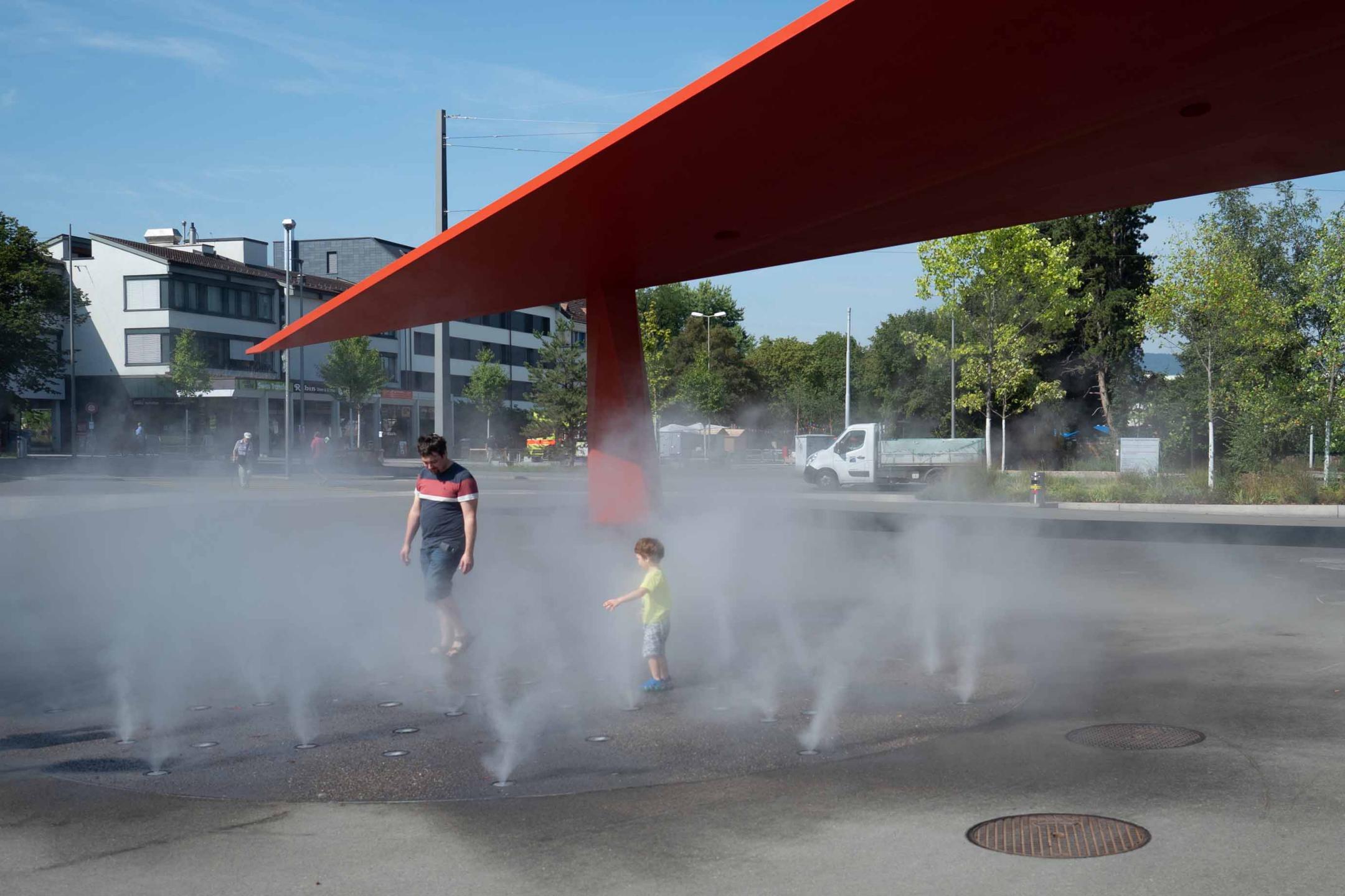 Schlieren, Stadtplatz: Eine Familie geniesst an einem heissen Sommertag die Kühle aus den Nebeldüsen.