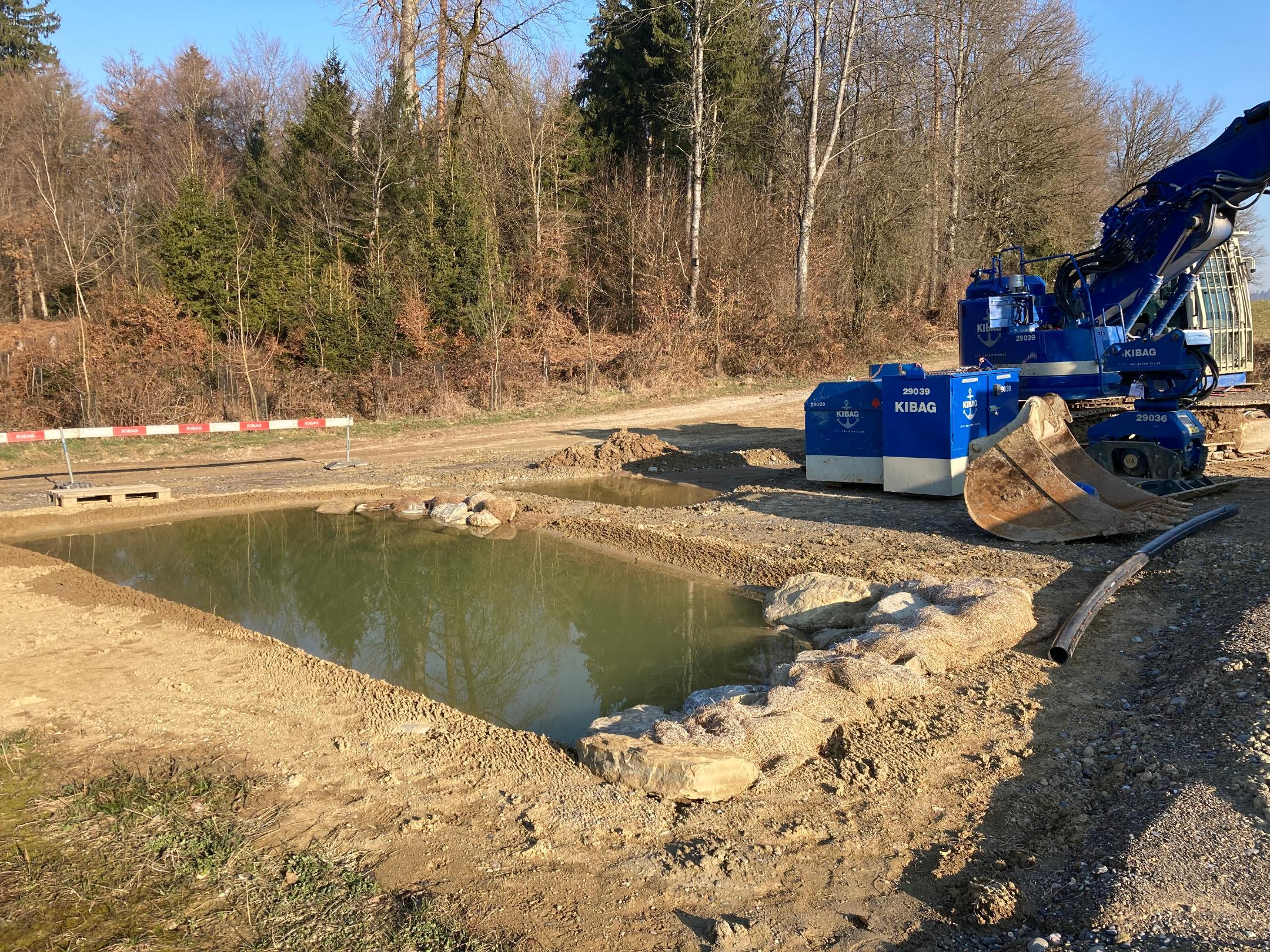 Bagger der einen rechteckigen Weiher, der bereits mit Wasser gefüllt ist, ausgehoben hat