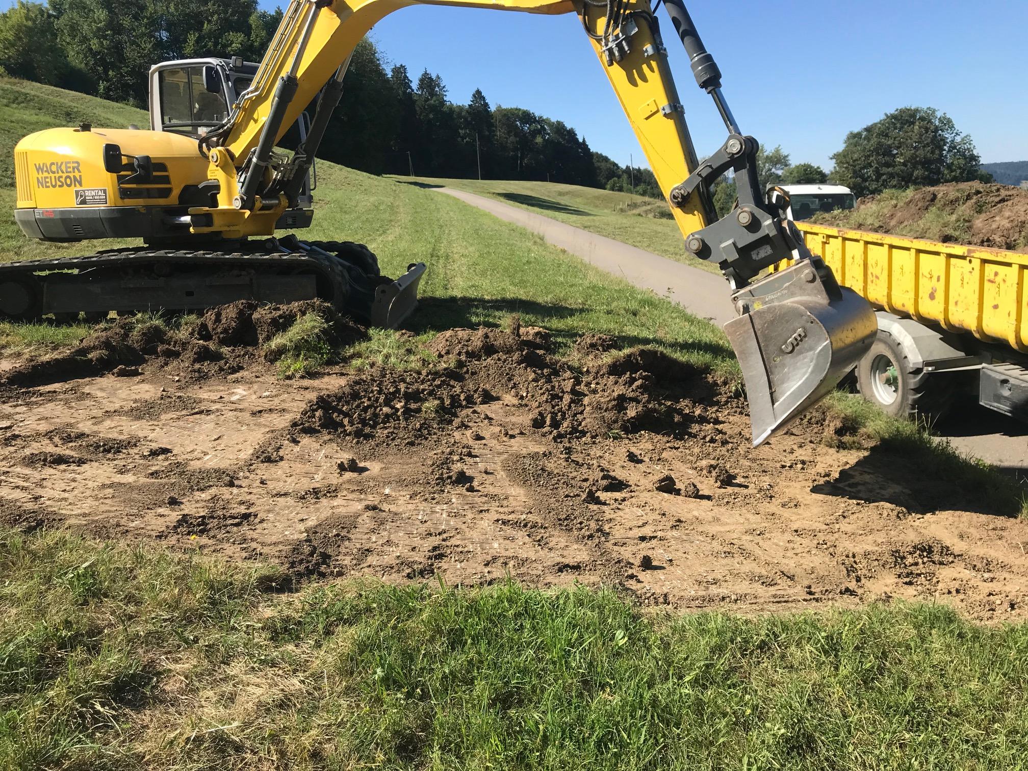 Ein gelber Bagger trägt den Oberboden ab