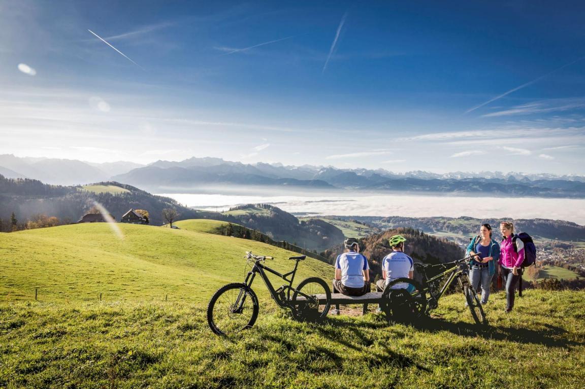 Velofahrer geniessen gemeinsam mit Wanderer den schönen Ausblick über die Alpen.