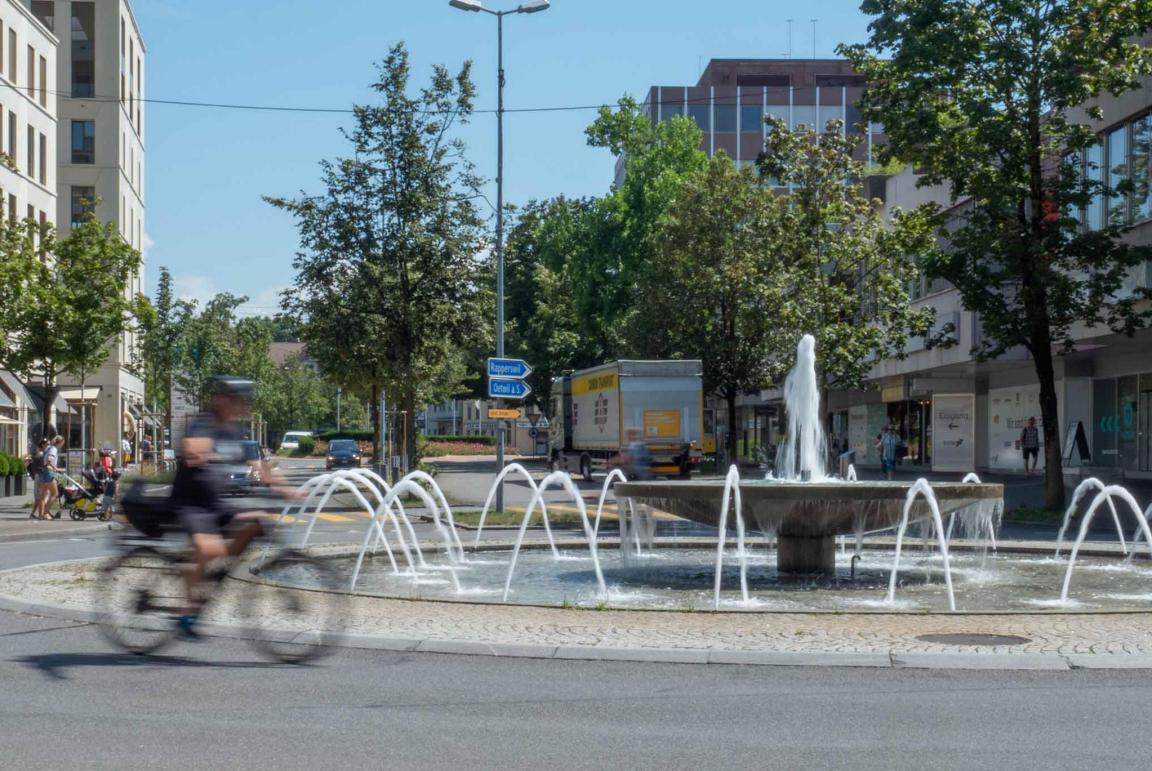 Bild zeigt einen grossen Brunnen der gleichzeitig der Verkehrsführung dient