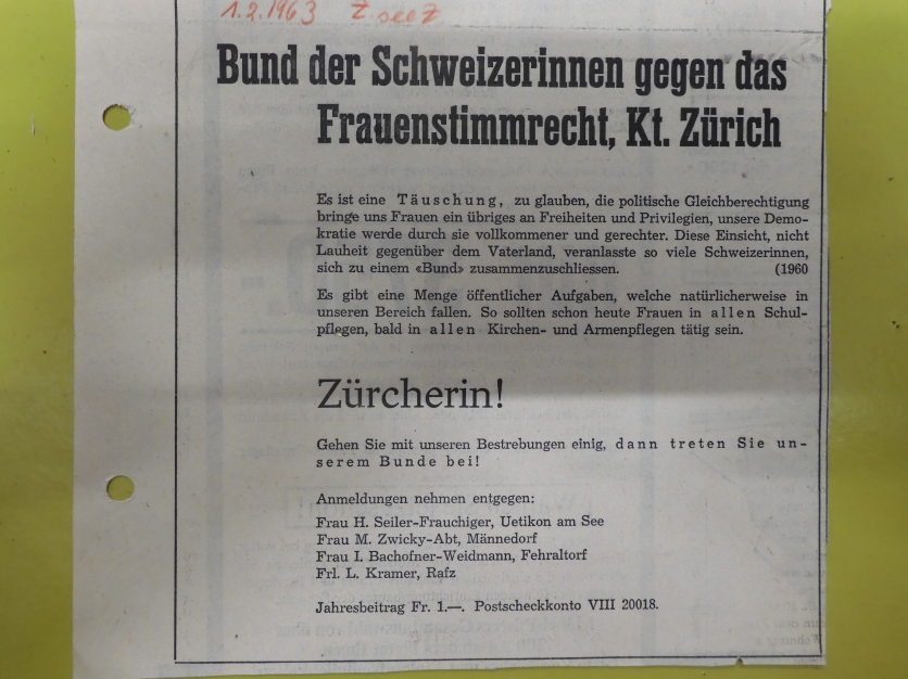 Ein altes schwarz-weiss fotografiertes Inserat, welche auf einem gelben Tisch liegt. Es appelliert gegen das Frauenstimmrecht.