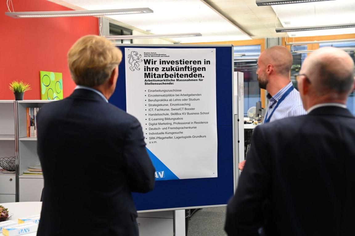 Drei Besucher betrachten ein Plakat mit dem Titel «Wir investieren in ihre zukünftigen Mitarbeitenden.»