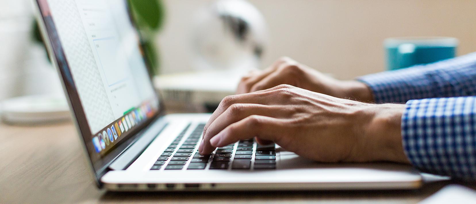 Hände eines Mannes tippen auf der Tastatur eines Laptops.