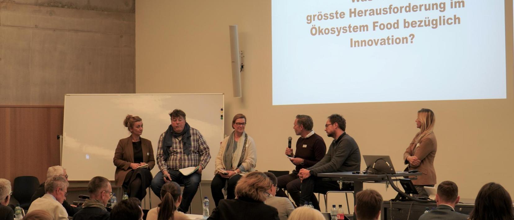 Fünf Panelisten und die Moderatorin in der Diskussion