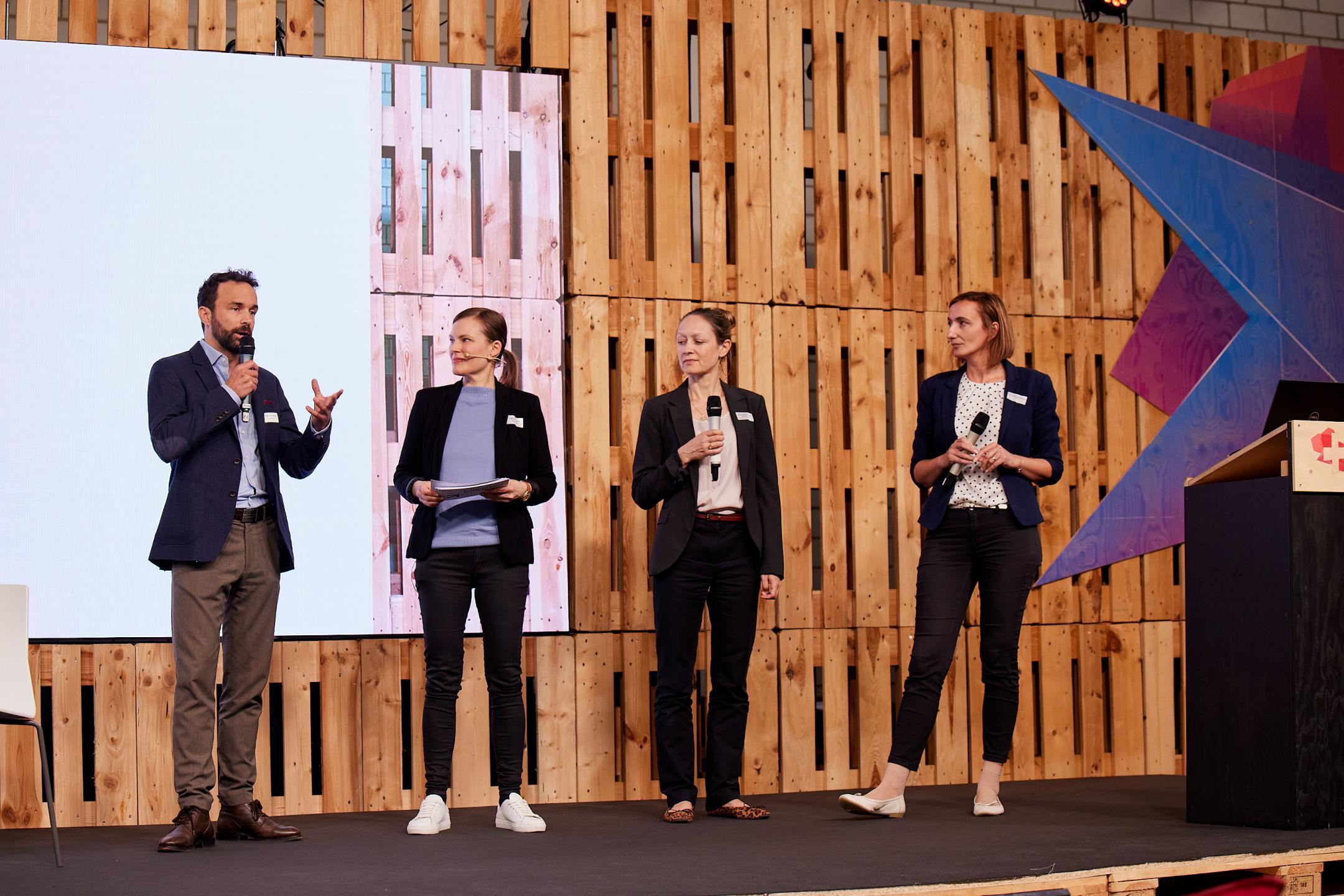 Ralph Schmidhalter von Innosuisse, Noémi Besedes als Moderatorin,  Anna-Julia Schlegel der ETH Zürich und Anca-Georgiana Rusu vom Innovation Booster Robotics stehen nebeneinander auf der Bühne und diskutieren. 