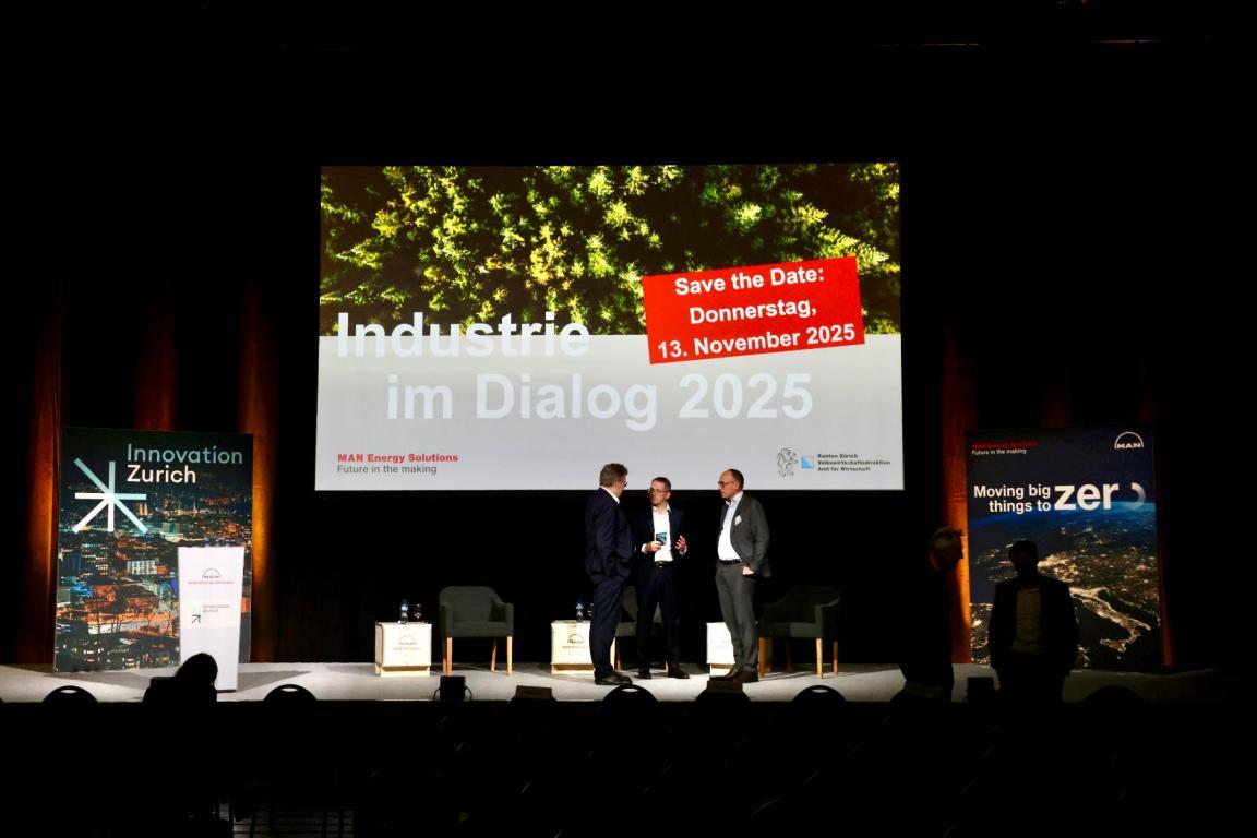 Drei Männer auf der Bühne. Hinter ihnen auf dem Bildschirm die Information «Industrie im Dialog 2025: Save the Date, Donnerstag, 13. November 2025»