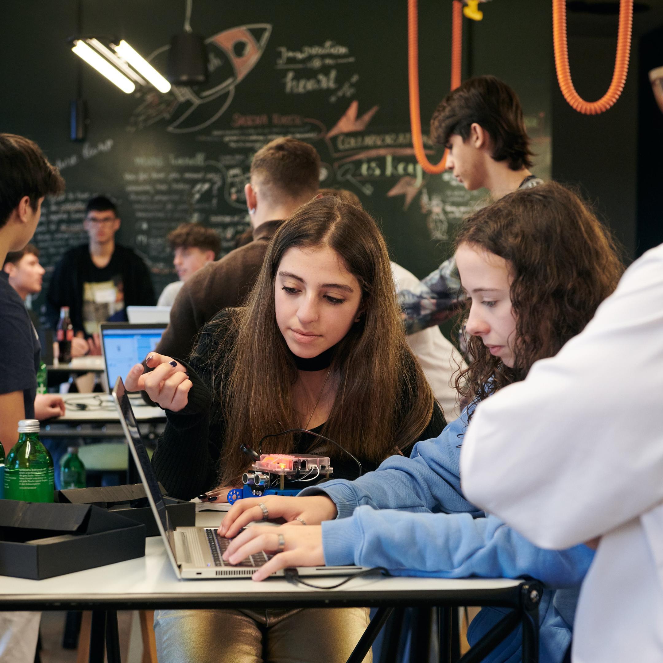 Zwei Mädchen sitzen an einem Tisch und schauen in einen Laptop