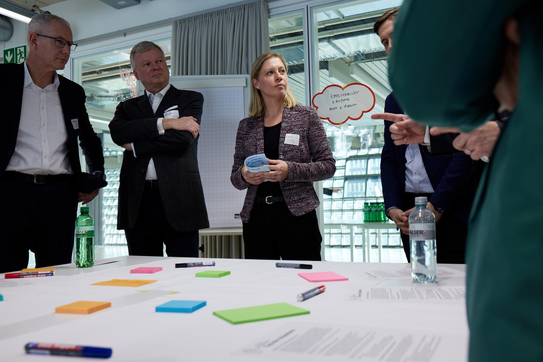 Mehrere Personen stehen um einen Tisch mit farbigen Zetteln und notieren sich Gedanken