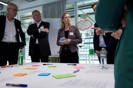 Mehrere Personen stehen um einen Tisch mit farbigen Zetteln und notieren sich Gedanken