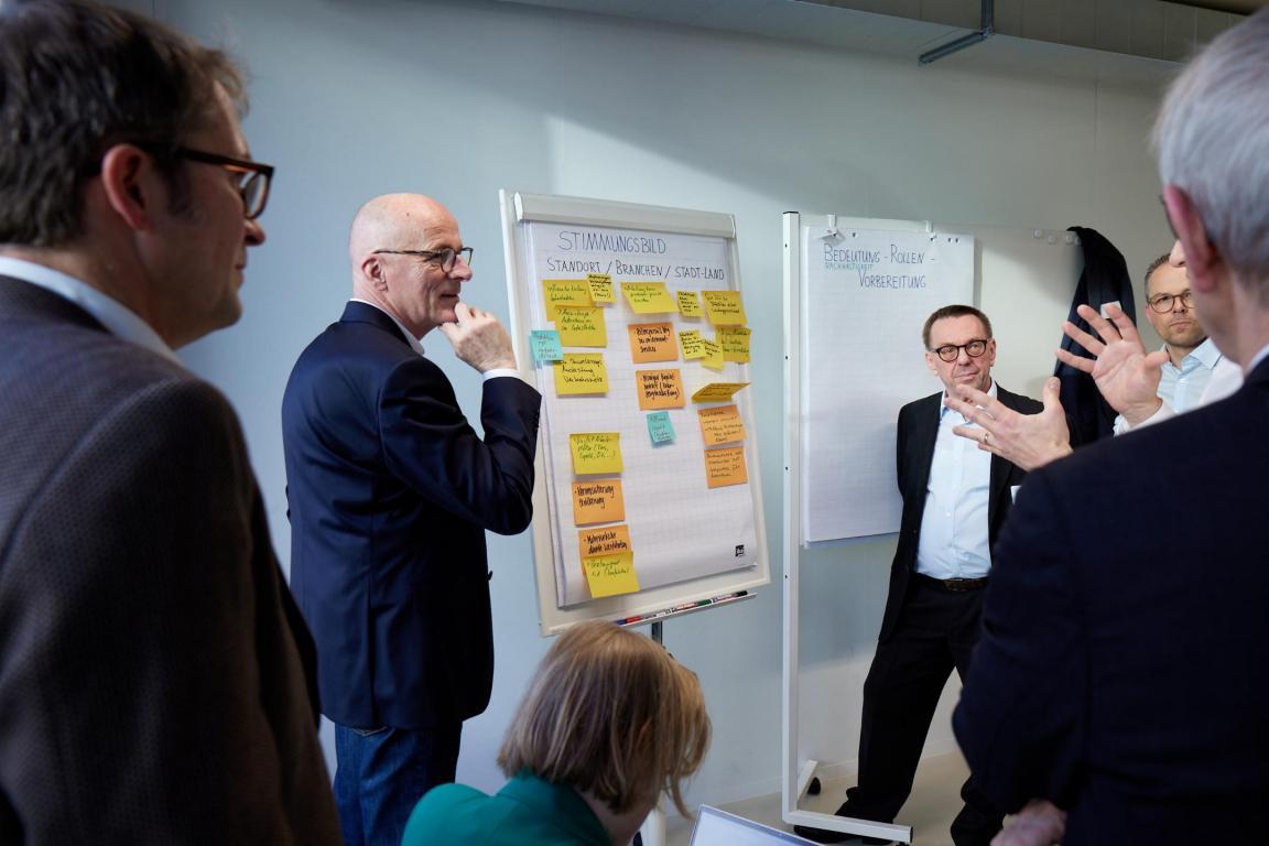 Mehrere Personen stehen um einen Flip-Chart und diskutiern miteinander