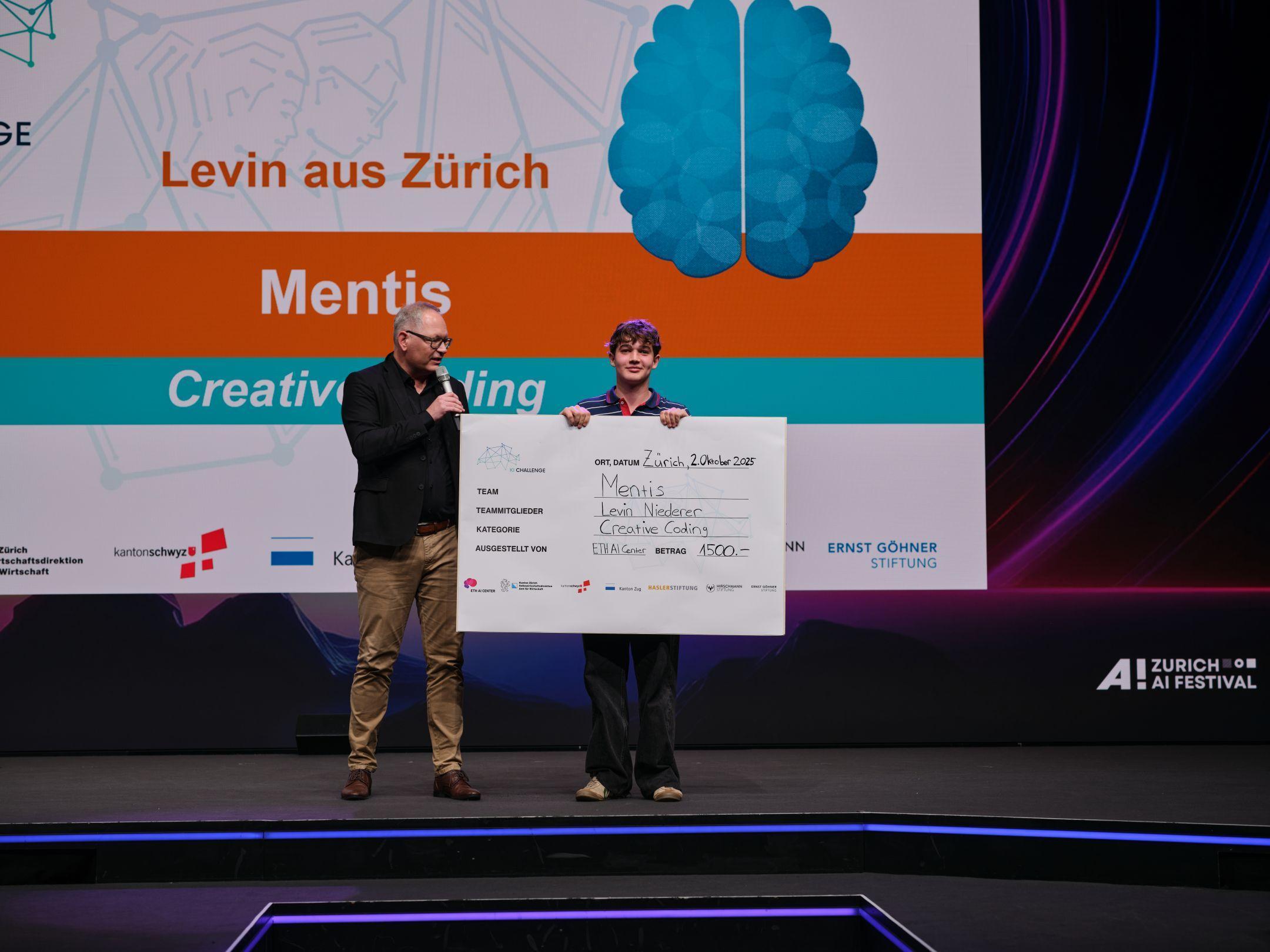 Levin Niederer steht mit Juror Daniel Stüssi auf der Bühne und hält einen grossen Scheck mit der Aufschrift «Mentis – Creative Coding» in den Händen.