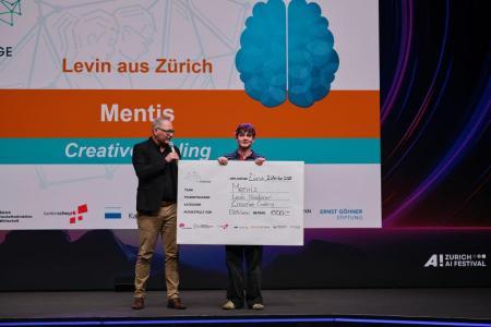 Levin Niederer steht mit Juror Daniel Stüssi auf der Bühne und hält einen grossen Scheck mit der Aufschrift «Mentis – Creative Coding» in den Händen.