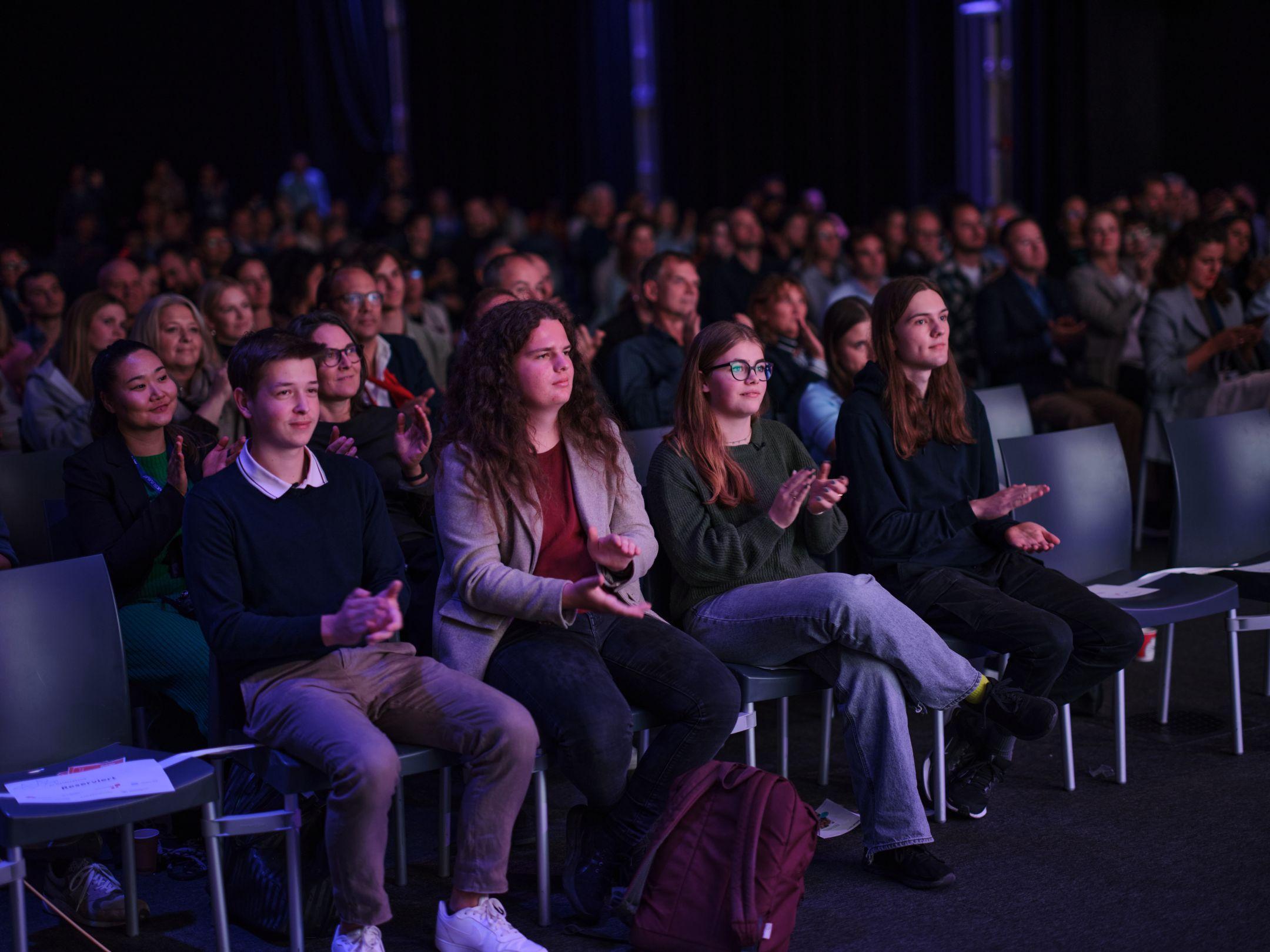 Menschen sitzen im Zuschauerraum und applaudieren während einer Veranstaltung des Zurich AI Festivals.