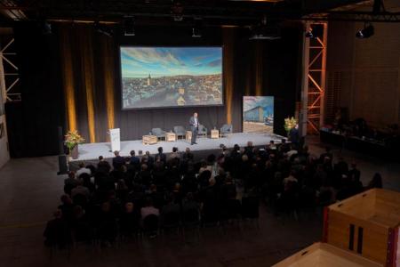 Michael Baumer steht auf der Bühne vor grossem Bildschirm mit Zürich-Panorama und spricht beim Event «Industrie im Dialog» in den Werkhallen von Everllence.