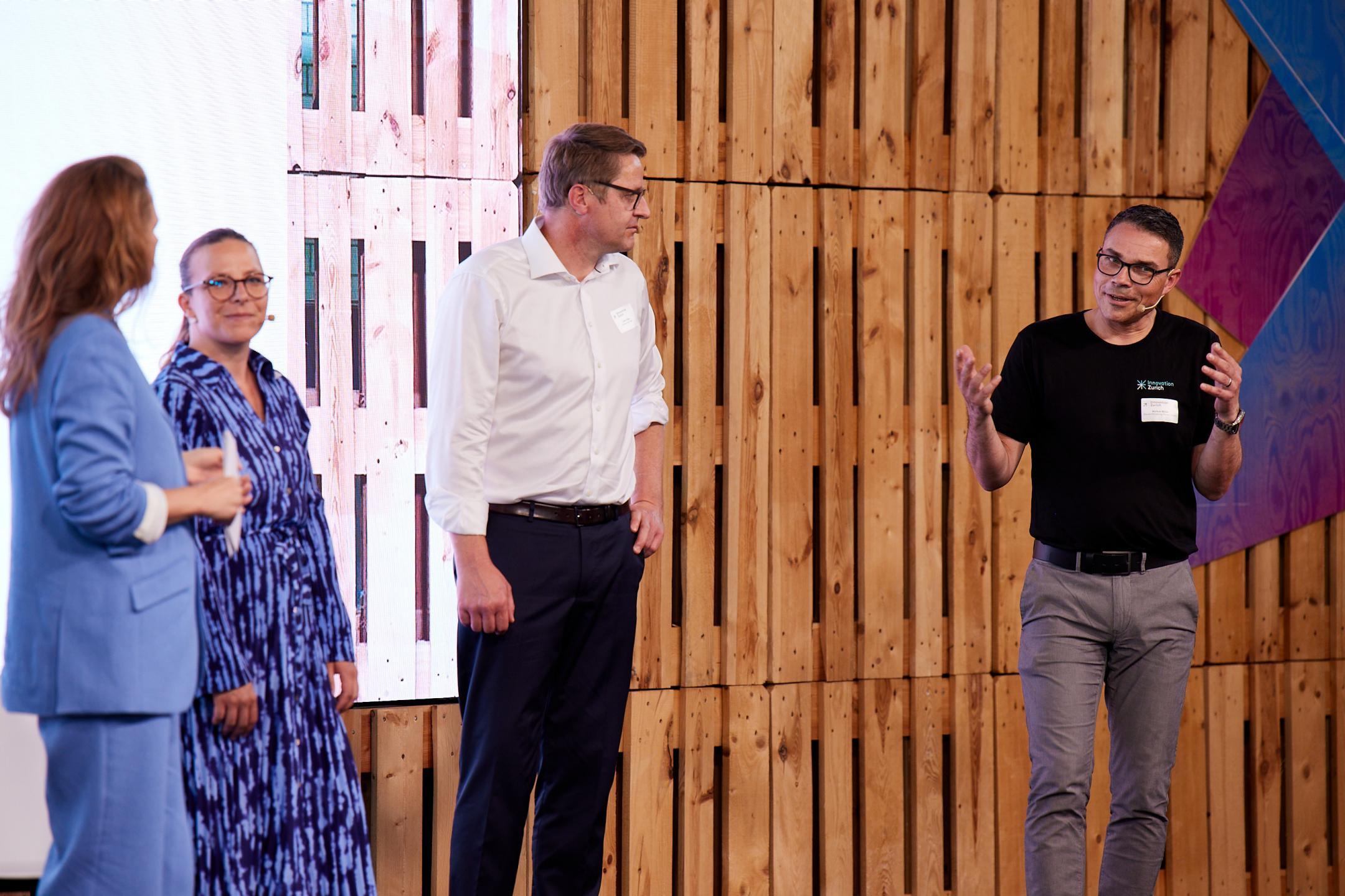 Kathrin Hönegger, Moderatorin, steht gemeinsam auf der Bühne mit Fabienne Kiener, Ad Interim Managing Director Foundation Switzerland Innovation Park Zurich, Lukas Huber, CEO der Greater Zurich Area, und Markus Müller, Co-Leiter der Standortförderung des Kantons Zürich. Bild: Tim Love Weber 