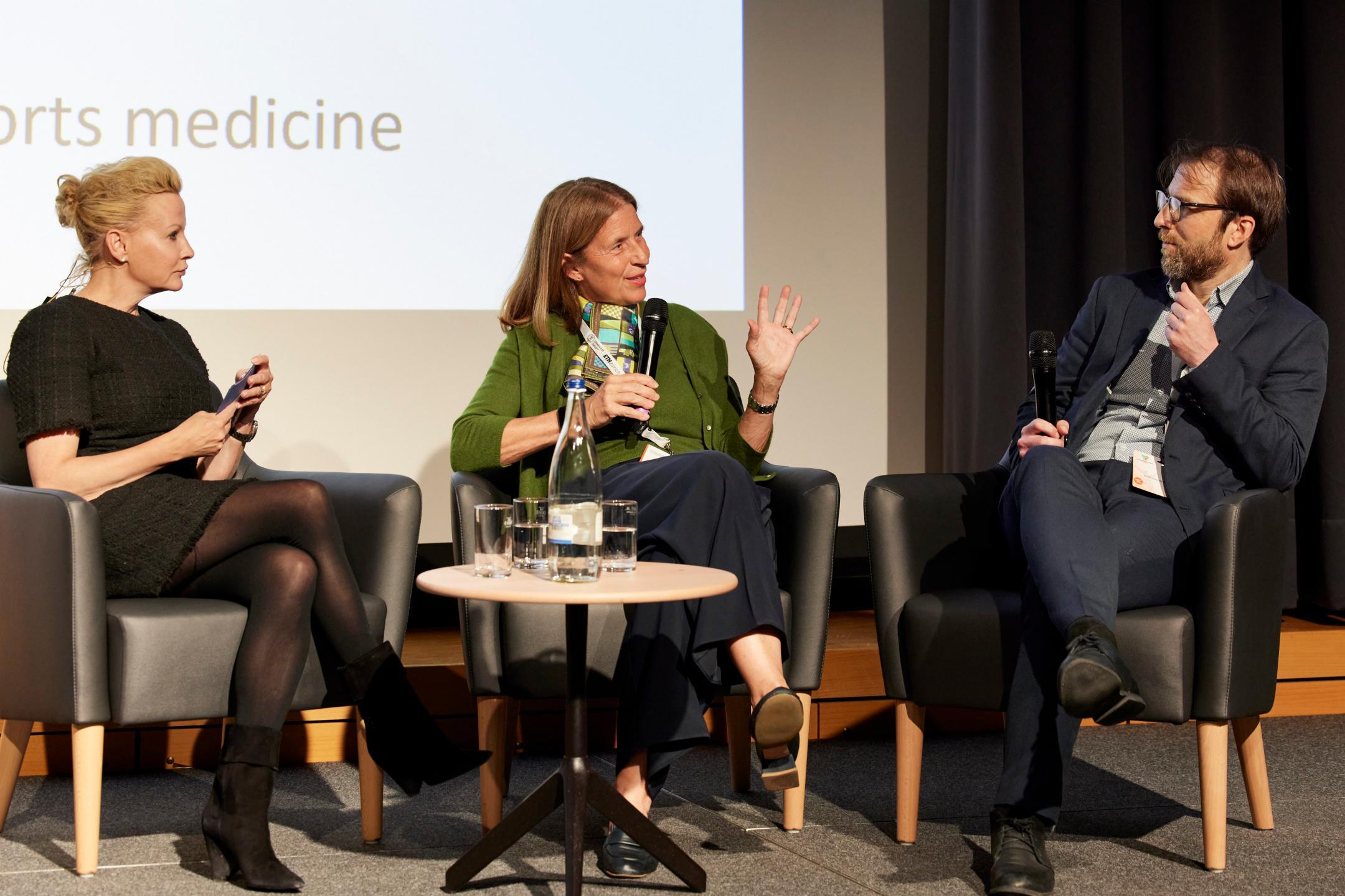 Prof. Beatrice Beck Schimmer spricht in das Mikrofon und sitzt zwischen der Moderatorin Dr. Anna Erat, links, und Prof. Thomas Ott auf der grossen Bühne. 