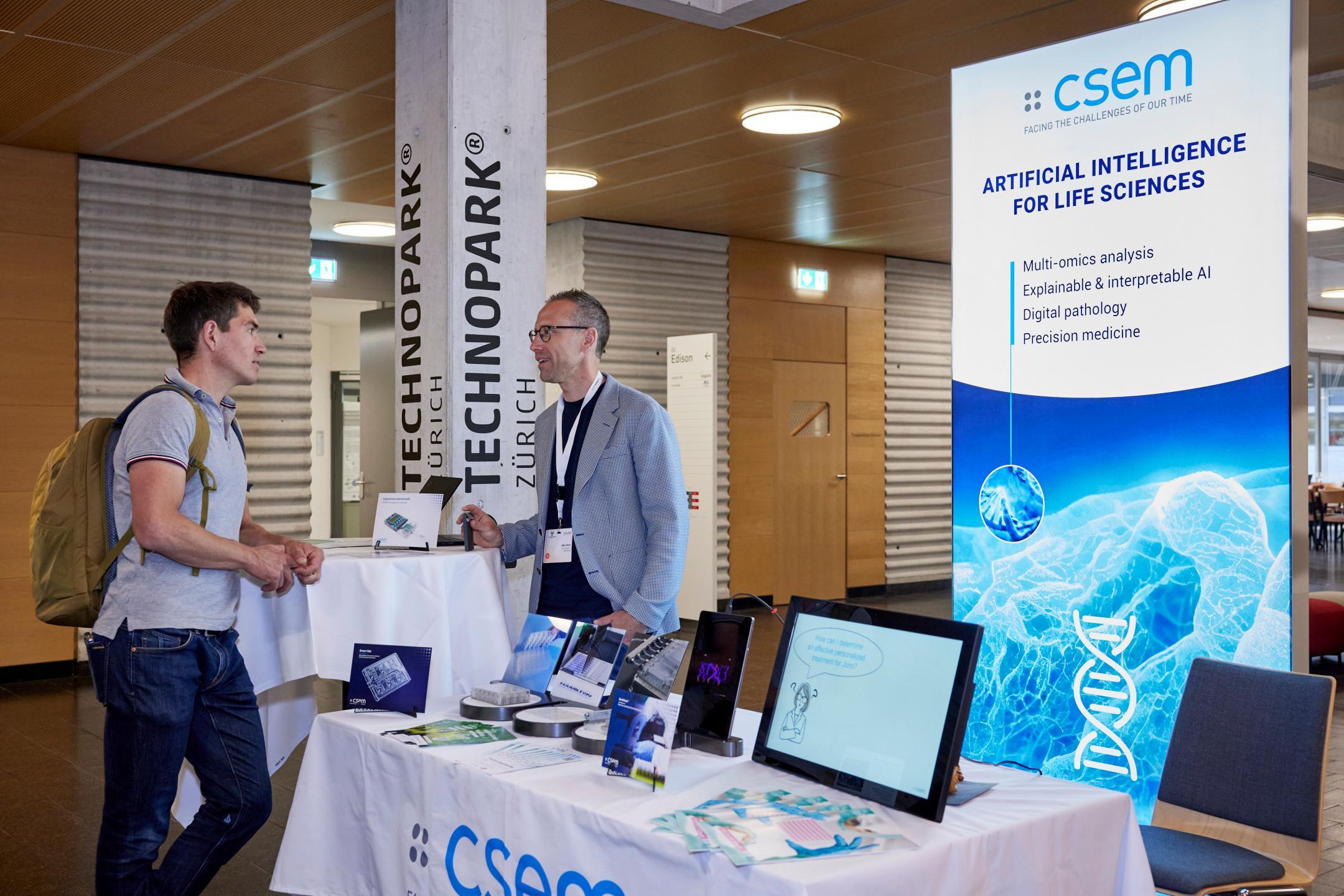 Links vom Ausstellerstand csem stehen zwei Herren und diskutieren.