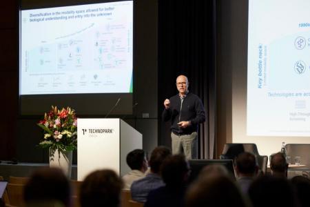Dr. Christian Rommel hält auf der Bühne des Technoparks Zürich seine Keynote. Im Hintergrund ist eine Folie unscharf zu erkennen.