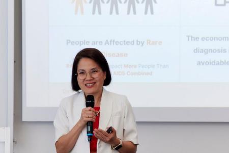 Dr. Quy Vo-Reinhard steht vor einer Leinwand und spricht lächelnd ins Mikrofon. Im Hintergrund sieht man unscharf einen Ausschnitt ihrer Präsentationsfolie.