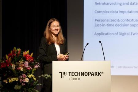 Dr. Susan Mérillat steht hinter dem weissen Rednerpult von Technopark Zürich auf der Bühne und spricht zum Publikum. Im Hintergrund ist ein kleiner Ausschnitt ihrer Präsentation zu sehen.