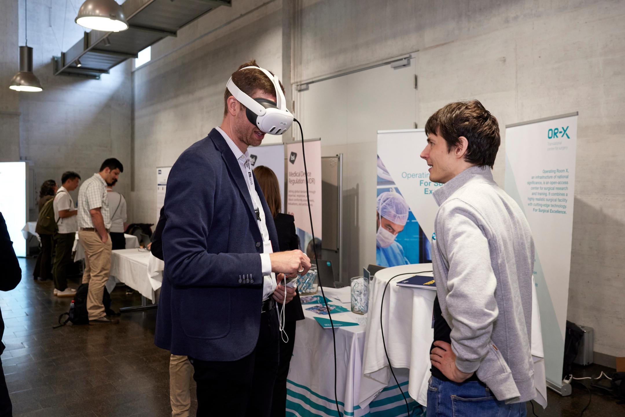 Ein Konferenzteilnehmer hat sich eine Virtual-Reality-Brille aufgesetzt. Ein Aussteller schaut ihn an.
