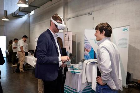 Ein Konferenzteilnehmer hat sich eine Virtual-Reality-Brille aufgesetzt. Ein Aussteller schaut ihn an.