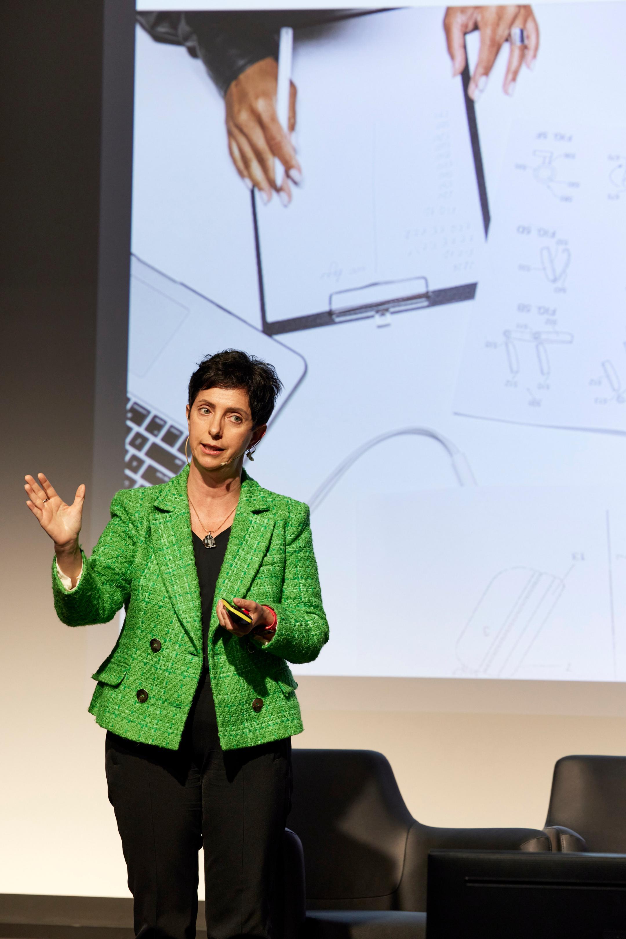 Jacqueline Ruedin Rüsch steht auf einer Bühne und referiert. Im Hintergrund ist ein Ausschnitt einer Präsentation zu sehen.