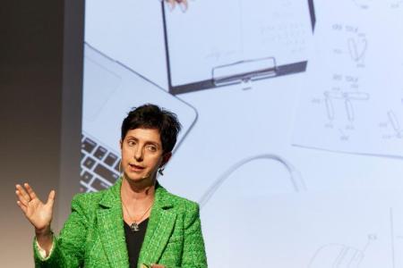 Jacqueline Ruedin Rüsch steht auf einer Bühne und referiert. Im Hintergrund ist ein Ausschnitt einer Präsentation zu sehen.