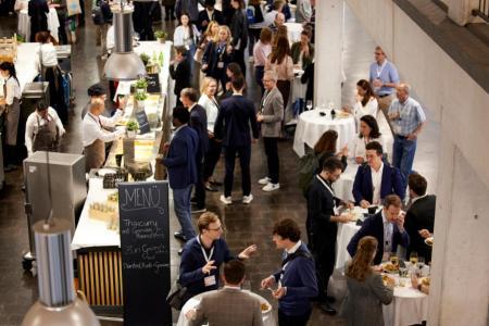 Blick von einer Galerie auf die Halle im Erdgeschoss des Technopark Zürichs.  Das Cateringbuffet ist eröffnet. Konferenzteilnehmende stehen verteilt an Hochtischen und geniessen den Stehlunch und tauschen sich aus.