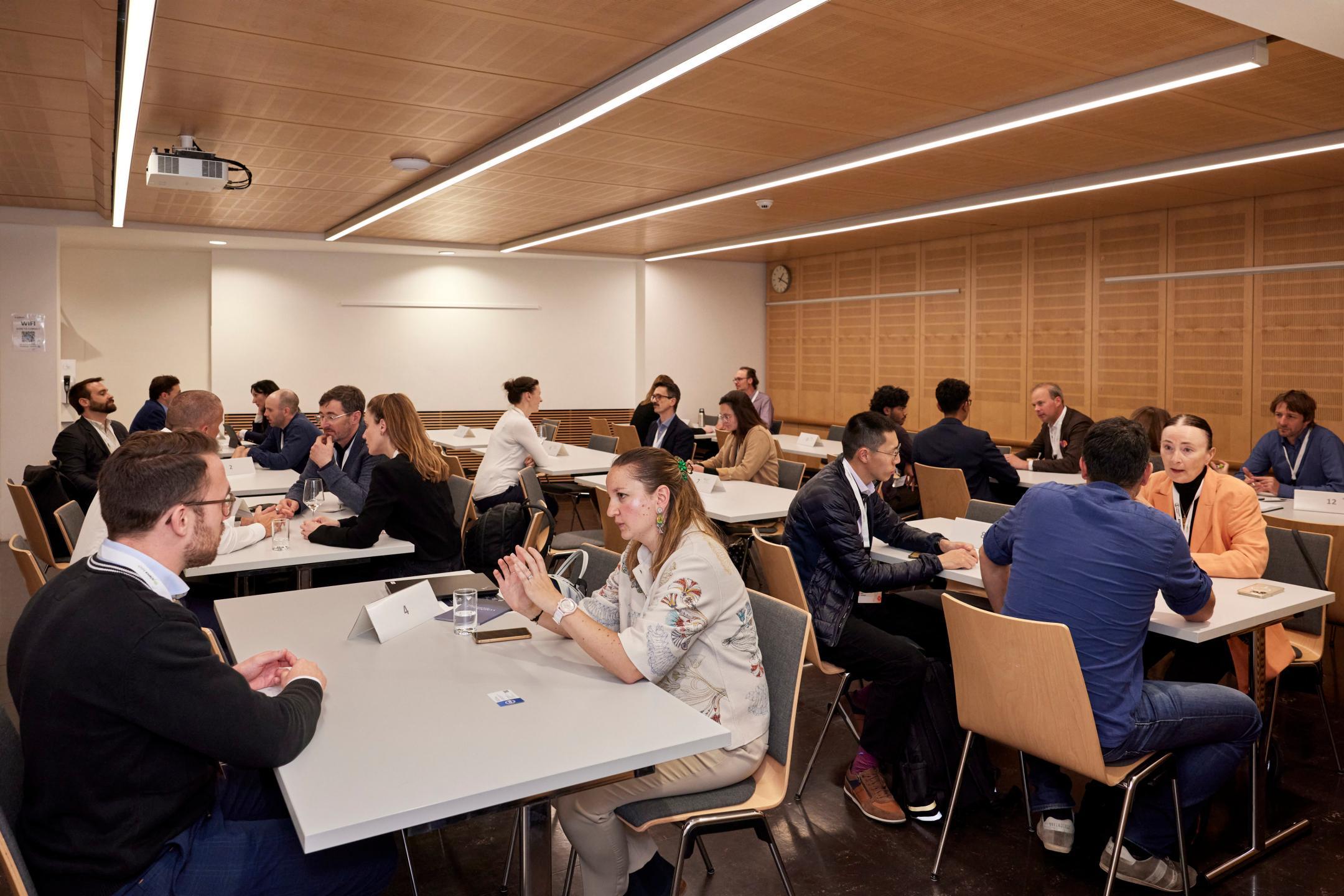 In einem Sitzungszimmer sieht man drei Tischreihen an denen 1:1 Gespräche zwischen zwei Personen geführt werden.