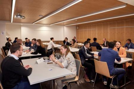 In einem Sitzungszimmer sieht man drei Tischreihen an denen 1:1 Gespräche zwischen zwei Personen geführt werden.