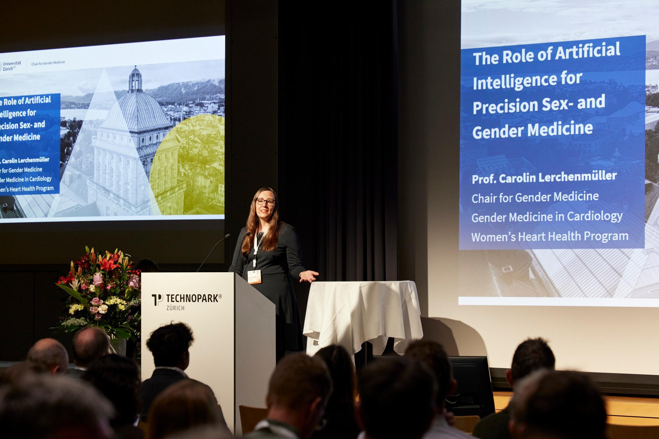 Prof. Carolin Lerchenmüller hält ihre Keynote auf der grossen Bühne. Thema gemäss der angezeigten Folie im Hintergrund: The Role of Artificial Intelligence for Precision Sex- and Gender Medicine.