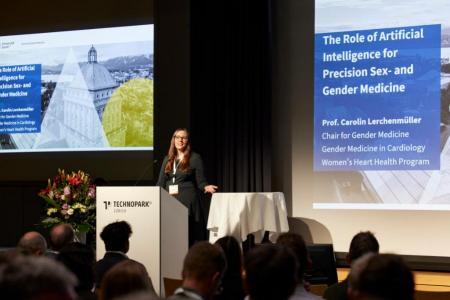 Prof. Carolin Lerchenmüller hält ihre Keynote auf der grossen Bühne. Thema gemäss der angezeigten Folie im Hintergrund: The Role of Artificial Intelligence for Precision Sex- and Gender Medicine.