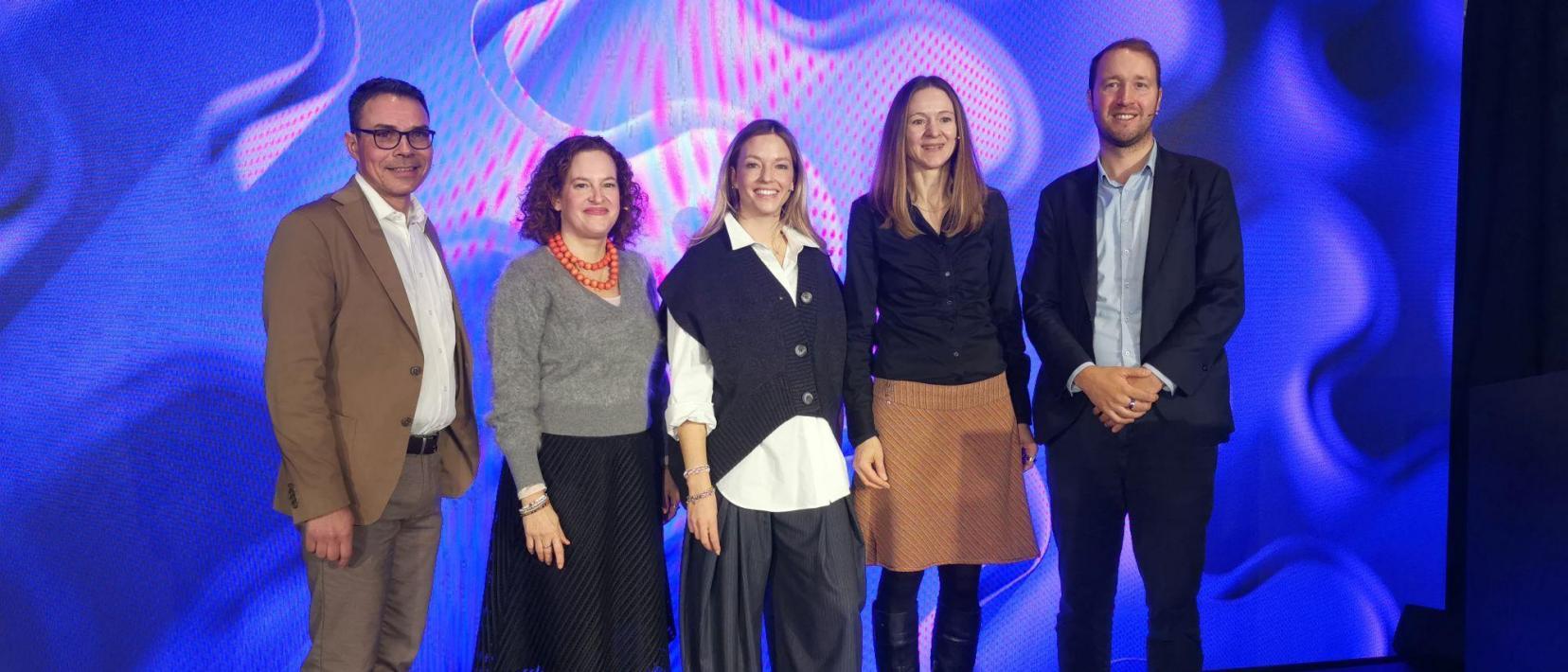 Fünf Personen stehen gemeinsam auf der Bühne vor einer blauen Präsentationswand mit dem open-i Logo bei der Innovationskonferenz in Zürich.