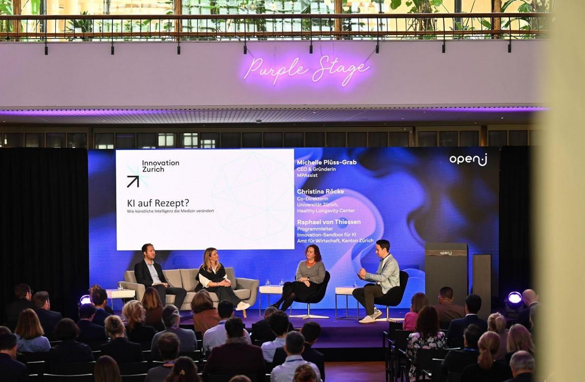 Vier Personen sitzen auf einer Bühne vor Publikum bei der Paneldiskussion «KI auf Rezept?» auf der Purple Stage der open-i Konferenz in Zürich. 