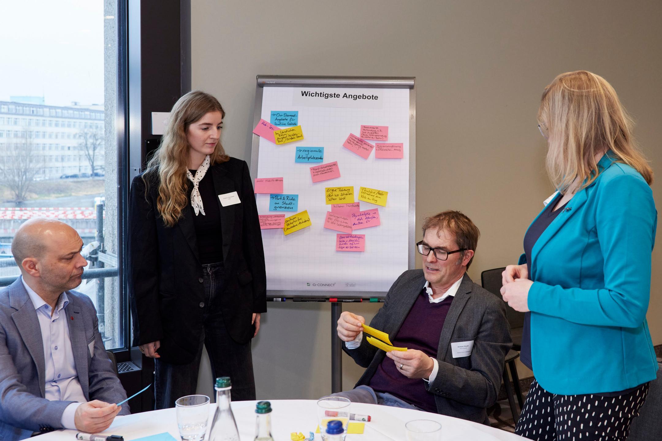 Teilnehmende diskutieren in einer Workshopgruppe vor einem Flipchart mit Haftnotizen.