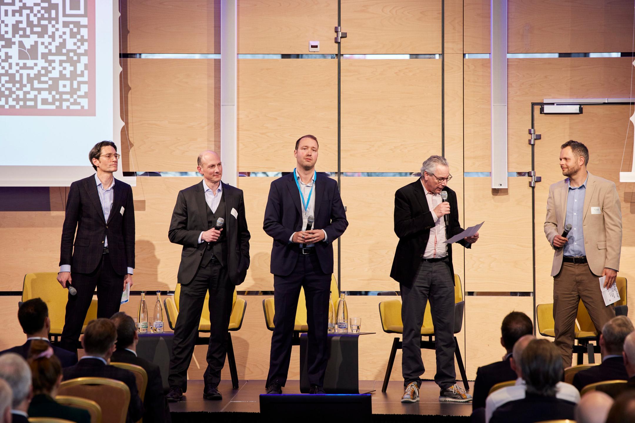 Mehrere Personen stehen auf der Bühne mit Mikrofonen und präsentieren Ergebnisse aus Workshops vor dem Publikum.